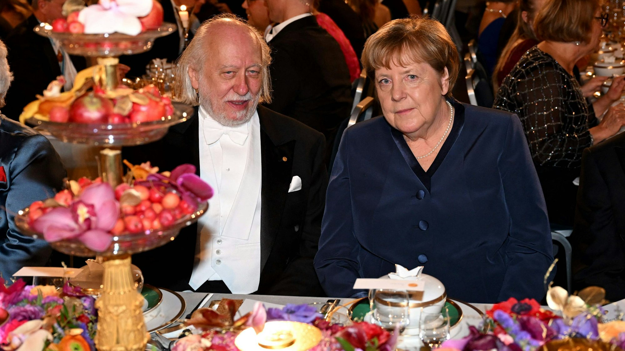 Die ehemalige deutsche Bundeskanzlerin Angela Merkel (2. v. r.) sitzt zwischen dem Preisträger des Sveriges Riksbank-Preises für Wirtschaftswissenschaften 2025, dem kanadischen Ökonomen Peter Howitt (r.), und dem Preisträger des Nobelpreises für Literatur 2025, dem ungarischen Schriftsteller László Krasznahorkai, beim Nobelpreis-Bankett am 10. Dezember 2025 im Rathaus von Stockholm, Schweden. Die Preisträger erhielten ihre Auszeichnungen am 10. Dezember im Rahmen feierlicher Zeremonien in Stockholm und Oslo. Dieser Tag ist der Todestag des Wissenschaftlers Alfred Nobel, der die Preise in seinem Testament gestiftet hatte.