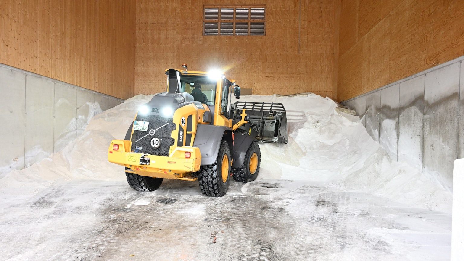 Ein Tieflader schaufelt einen großen weißen Berg aus Streusalz in einer Halle zusammen.