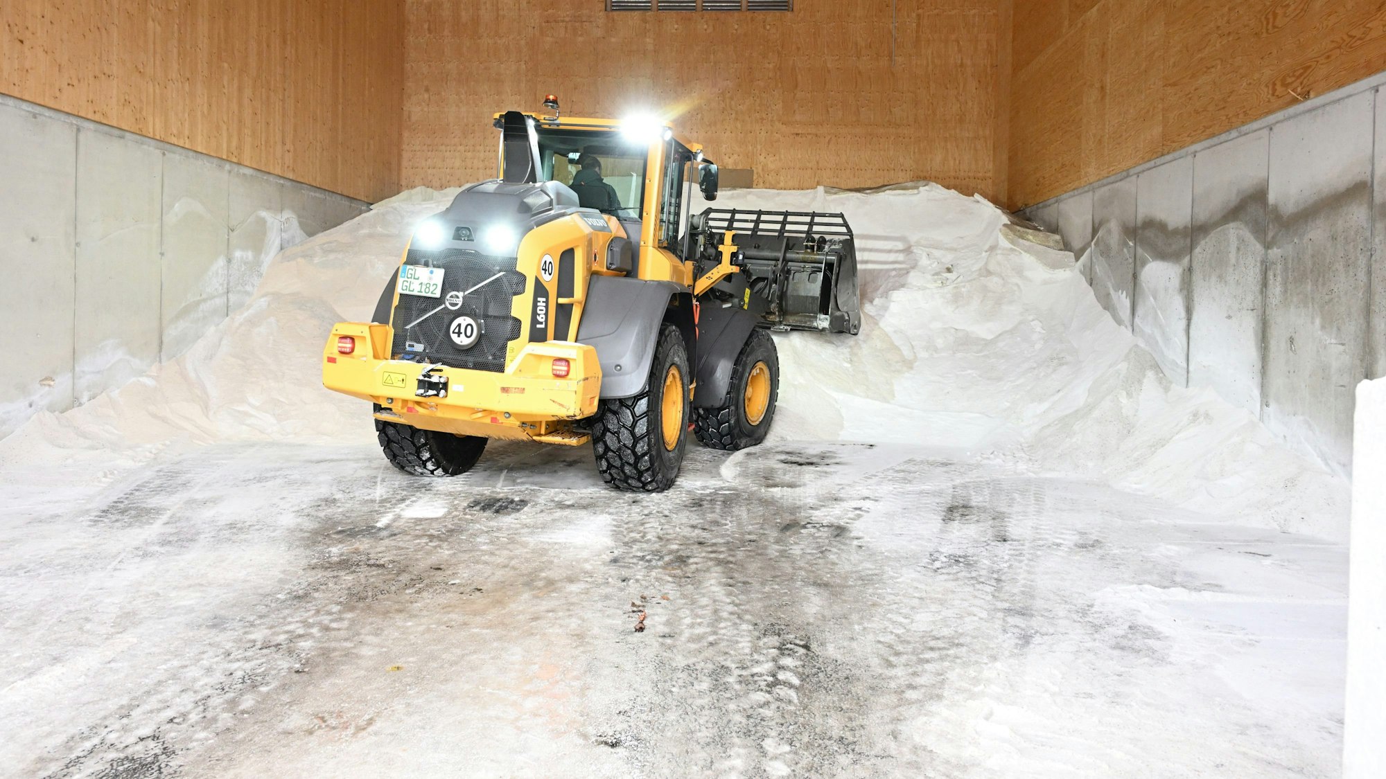 Ein Tieflader schaufelt einen großen weißen Berg aus Streusalz in einer Halle zusammen.
