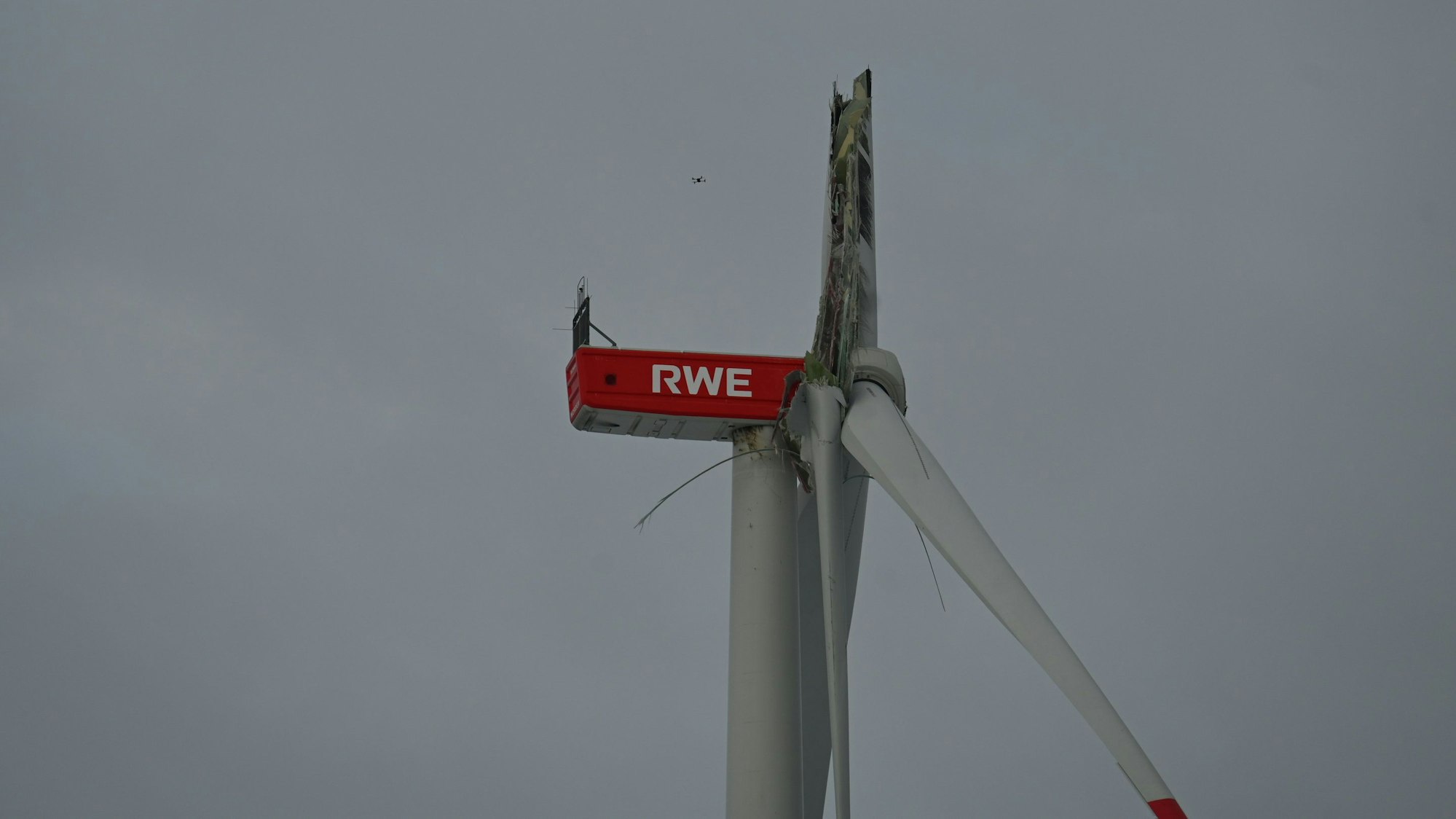 Das Bild zeigt die beschädigte Windkraftanlage. Eines der Rotorenblätter ist nach unten abgeknickt. Auf der Anlage ist der Schriftzug „RWE“ zu sehen.