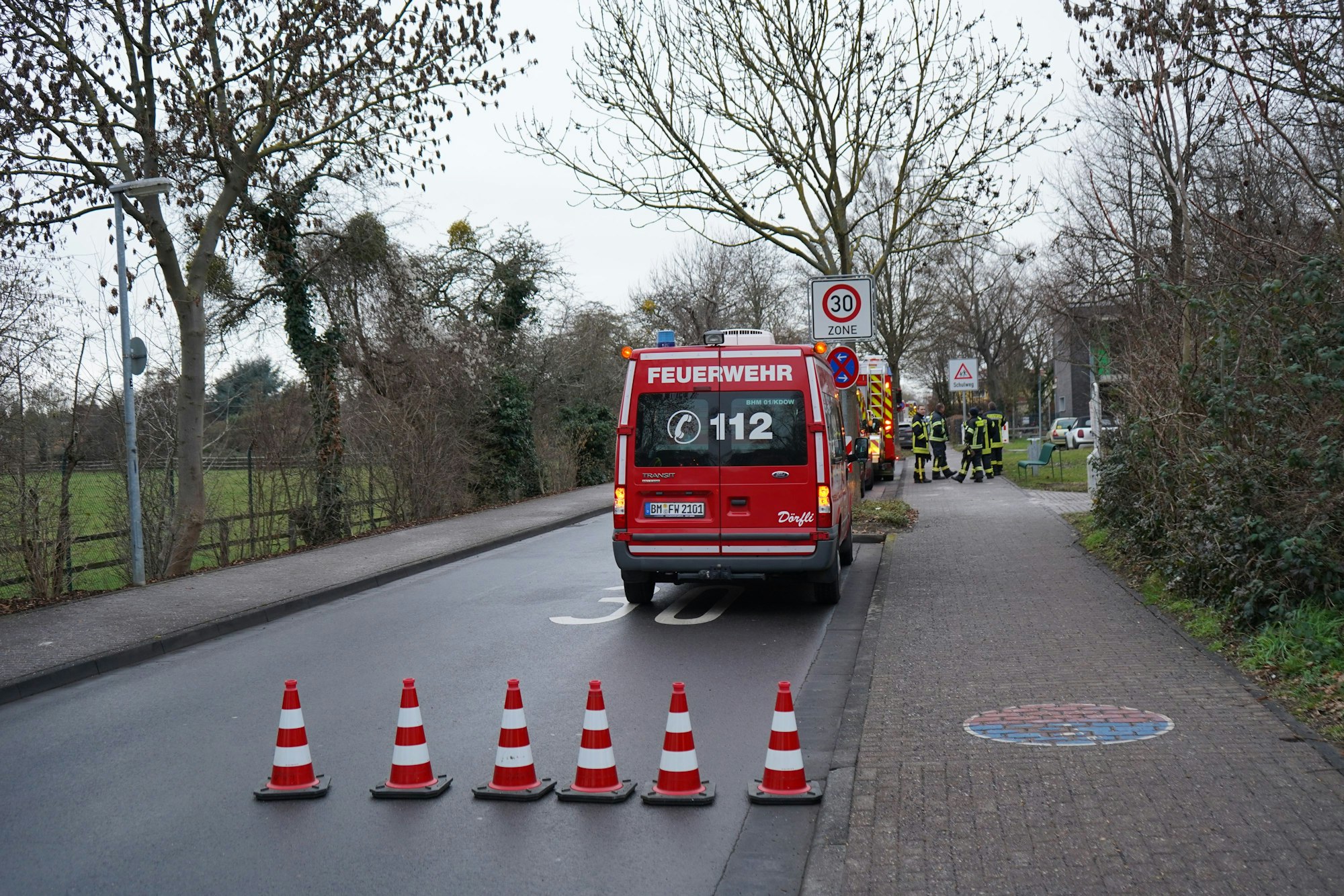 Das Bild zeigt rot-weiß gestreifte Leitkegel und Feuerwehrautos an der Absperrung.