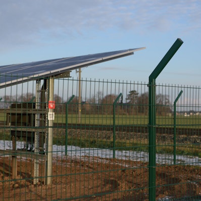 Ein Solarmodul hinter einem Zaun ist zu erkennen, dahinter der Ratsheimer Hof bei Kuchenheim.