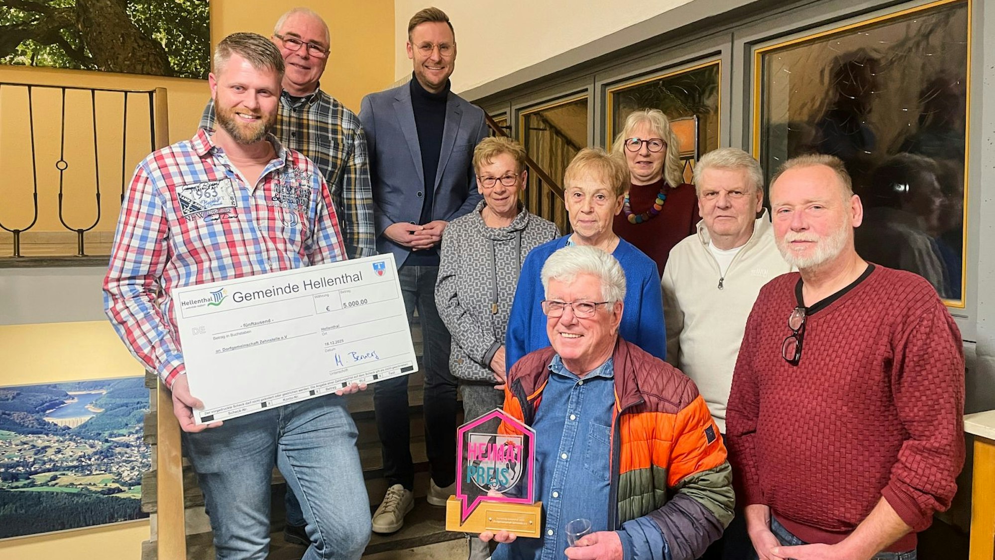 Neun Menschen haben sich zum Gruppenbild versammelt. Ein Mann hält einen überdimensionalen Scheck in den Händen, ein anderer einen Preis.