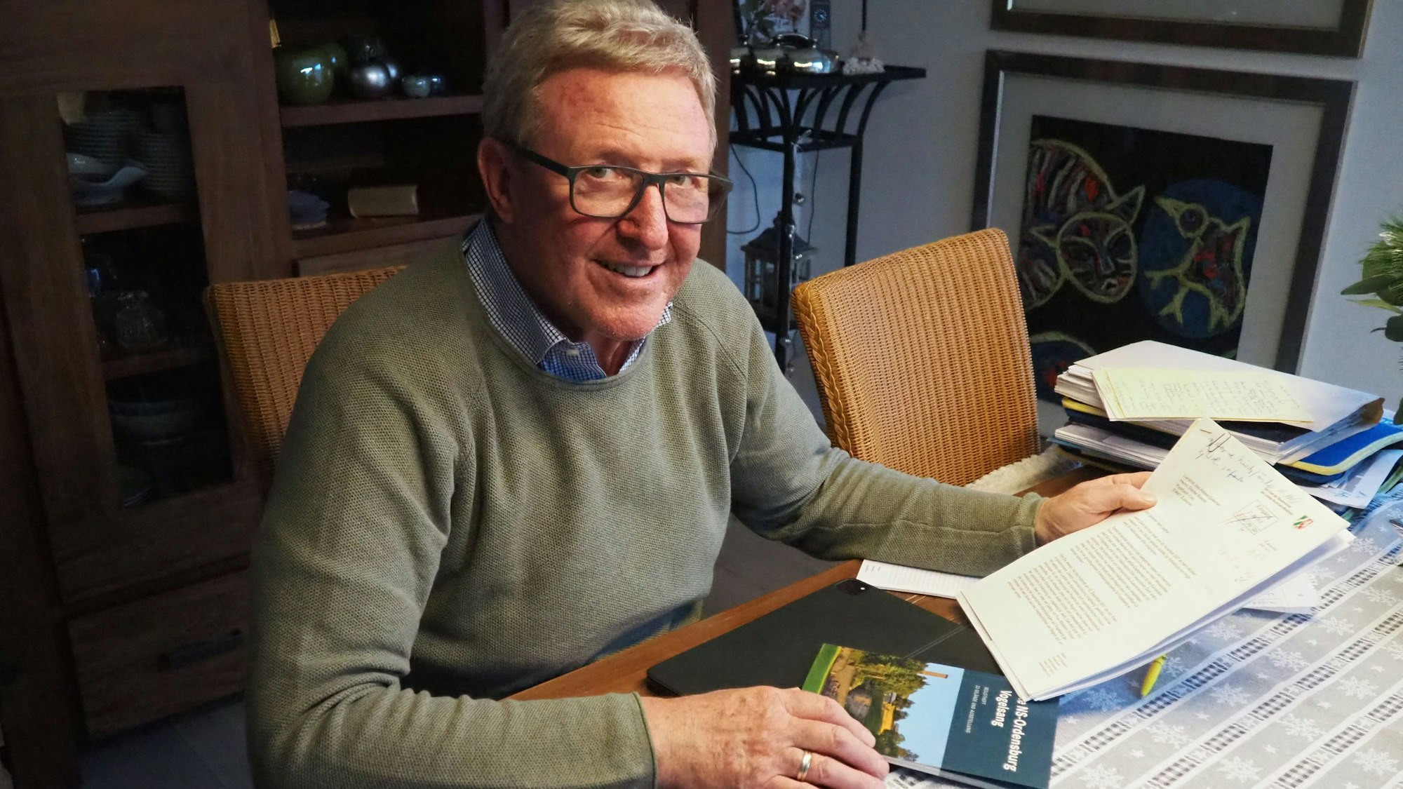 Manfred Poth sitzt am Tisch und hält Papiere in der Hand.