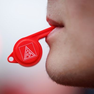 Ein Arbeiter mit Trillerpfeife (IGM) steht bei einer Kundgebung der IG Metall vor einem Betriebsgelände.