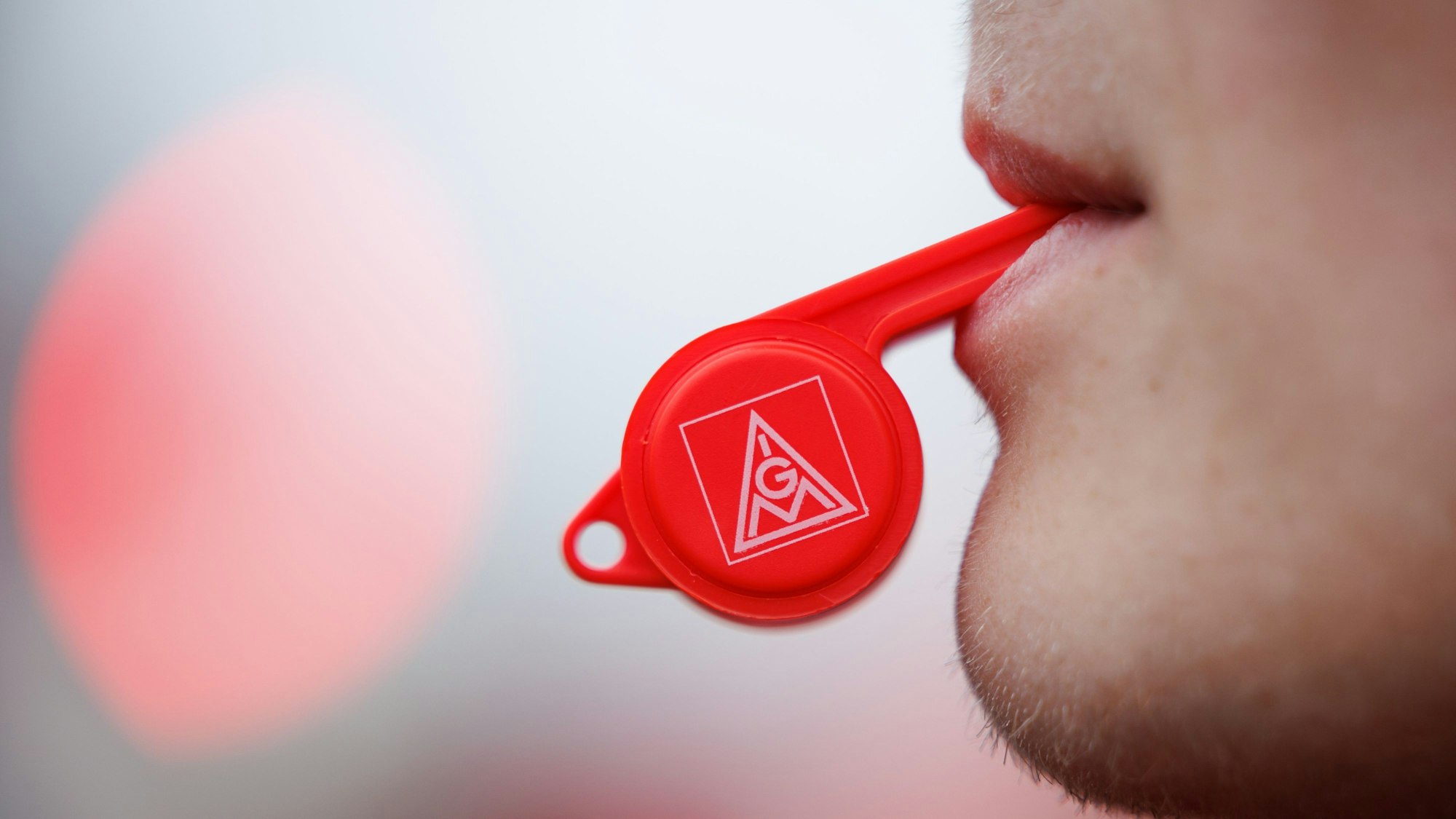 Ein Arbeiter mit Trillerpfeife (IGM) steht bei einer Kundgebung der IG Metall vor einem Betriebsgelände.