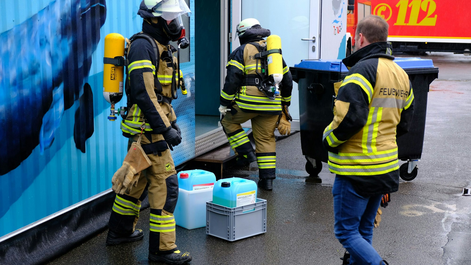 Drei Feuerwehrleute - zwei mit Atemschutz - haben Kanister mit einer Chlorgasflüssigkeit aus einem blauen Schwimmcontainer geborgen.