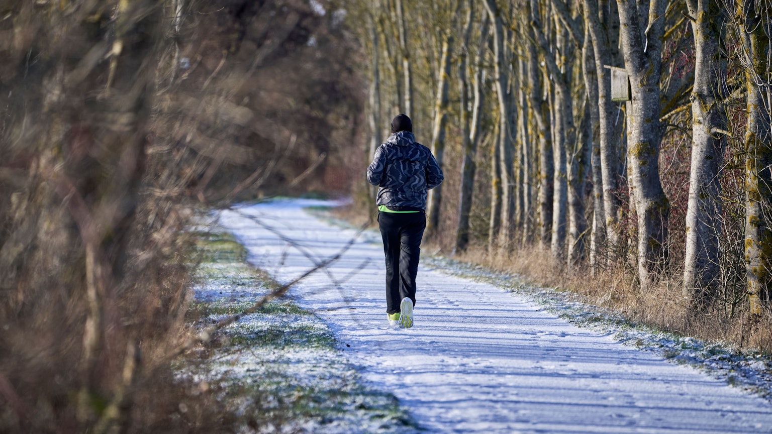 Ein Freizeitsportler joggt durch eine leicht verschneite Winterlandschaft.
