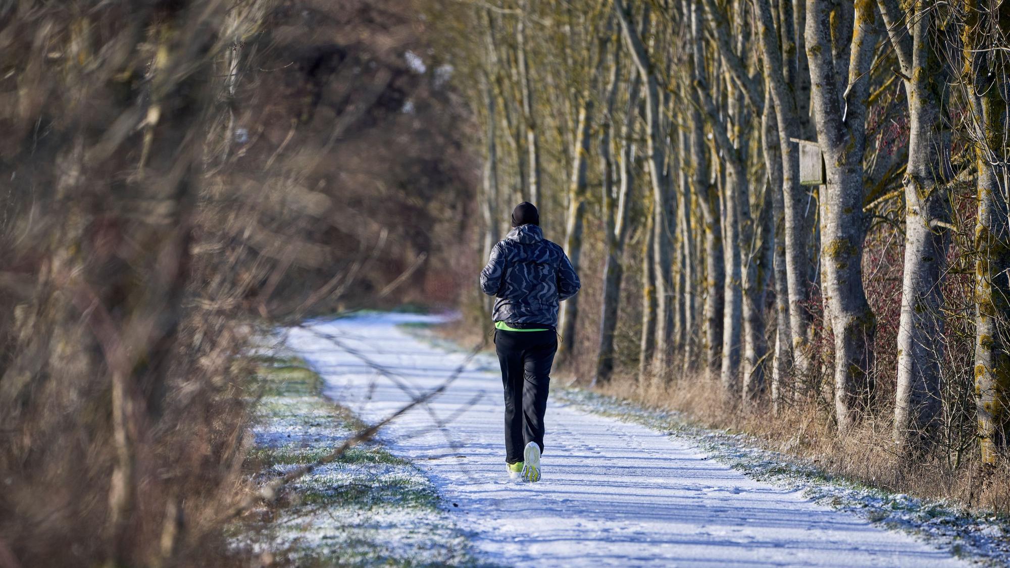 Ein Freizeitsportler joggt durch eine leicht verschneite Winterlandschaft.