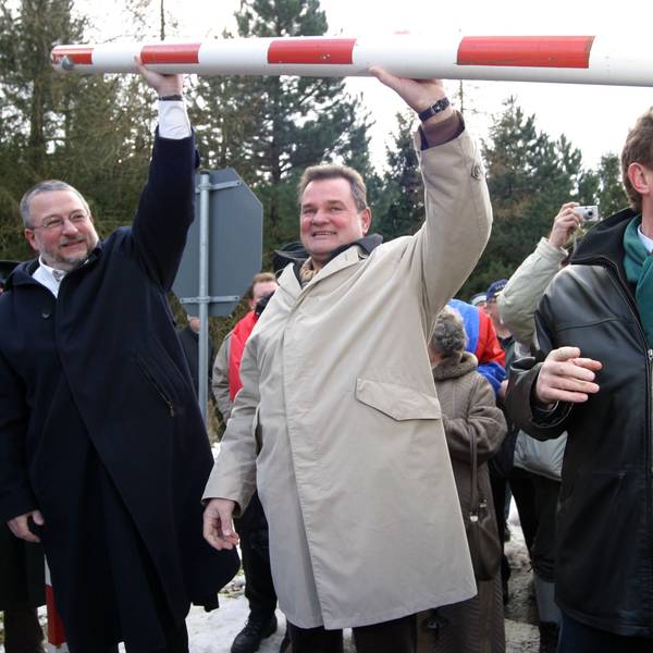 Ralf Hergarten, Günter Rosenke und Manfred Poth heben den Schlagbaum über ihre Köpfe.Im Hintergrund sind andere Menschen zu sehen.