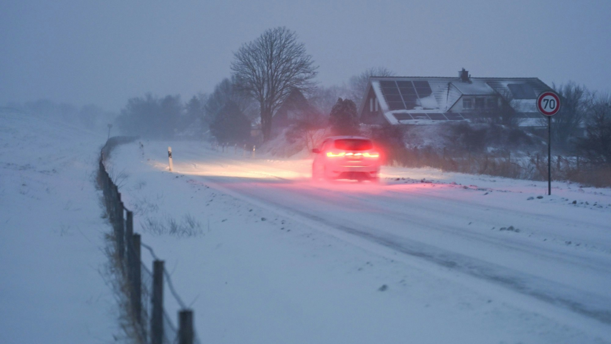 Das Bild zeigt eine schneebedeckte Straße am Deich in Niedersachsen, Moormerland. Foto: Lars Penning/dpa