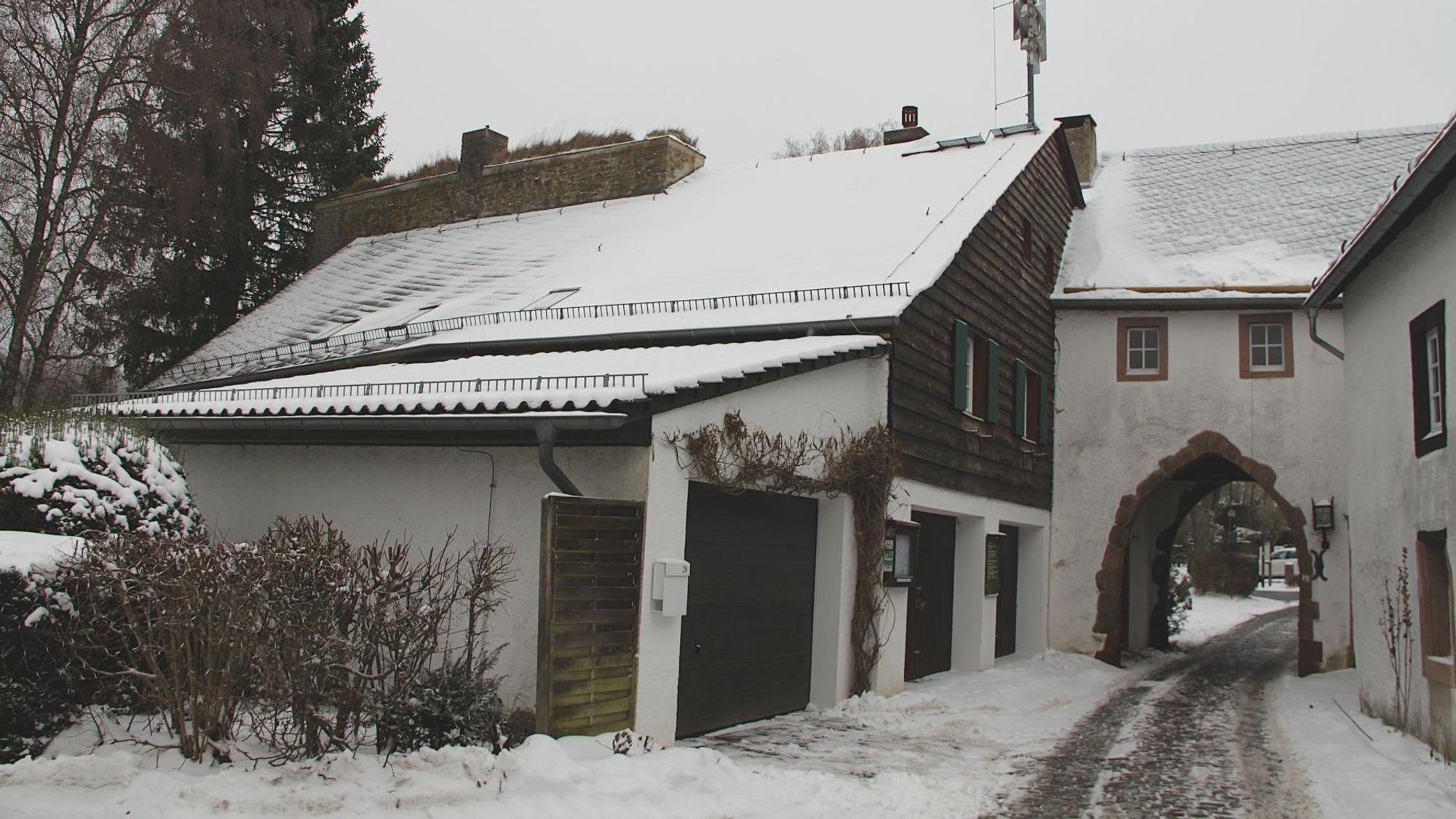Nahe eines Tors des Burgberings in Kronenburg befindet sich ein Haus, an das eine Garage angebaut ist. Auf den Dächern liegt Schnee.