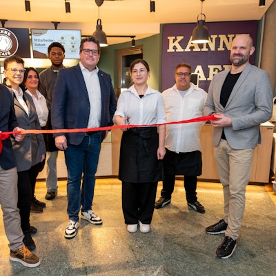 Sebastian Haeger (Geschäftsführer Gesundheitscampus Quirlsberg), der Area Manager von Kanne Café Andreas Brachem und das Team des Cafés schneiden zur Eröffnung im EVK ein rotes Band durch.