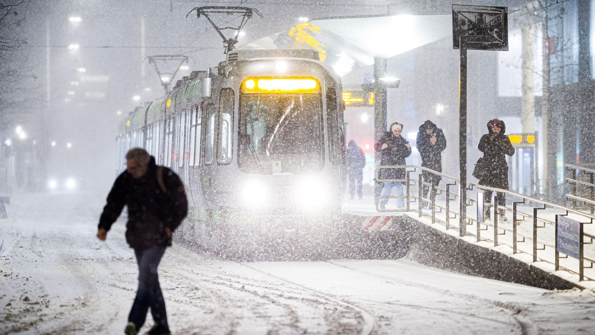 Das Bild zeigt eine Straßenbahn am frühen Morgen im dichten Schneefall an einer Haltestelle im Zentrum von Hannover. Foto: Moritz Frankenberg/dpa