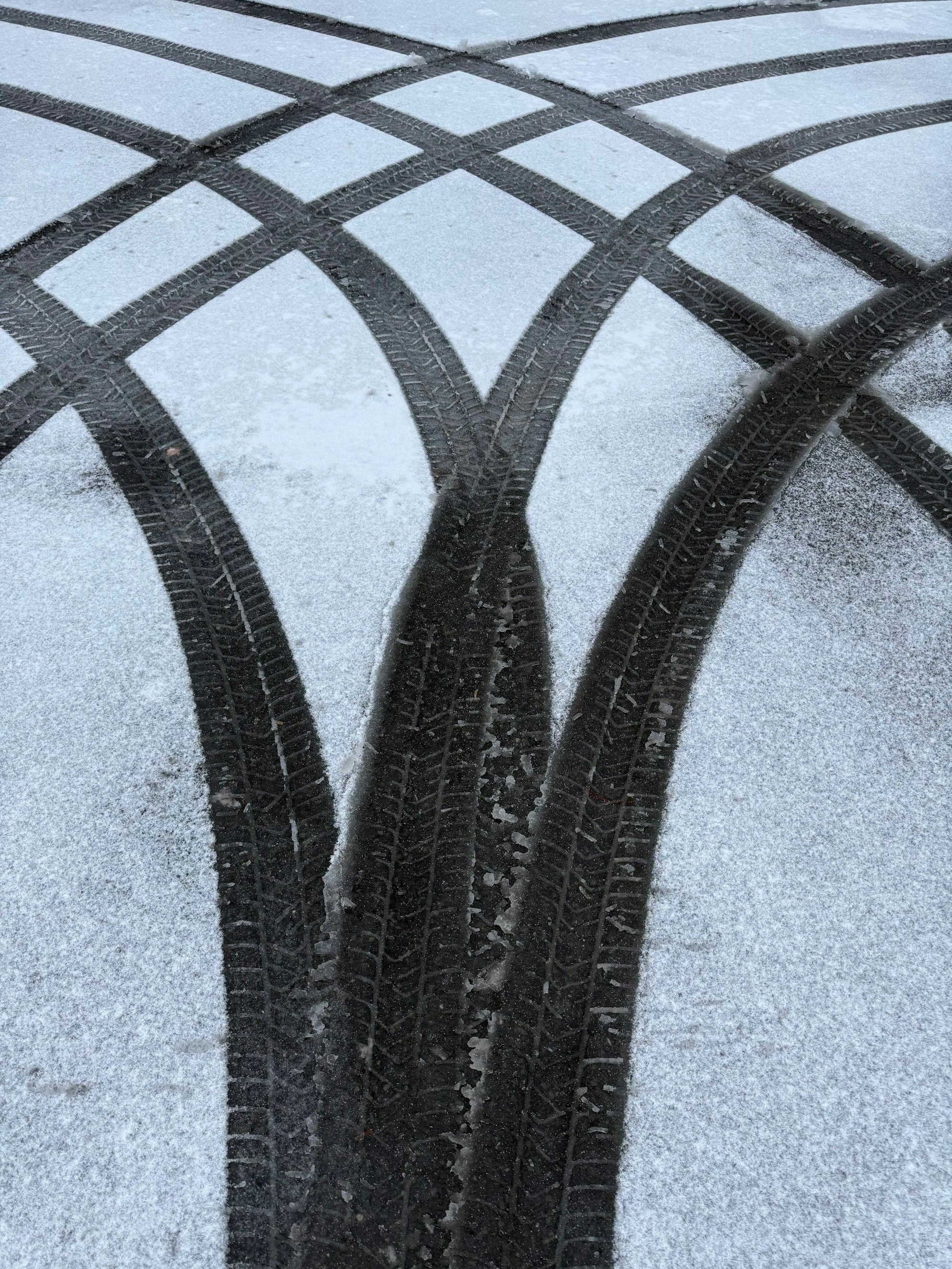 Das Bild zeigt Reifenspuren im Schnee auf einem Parkplatz.