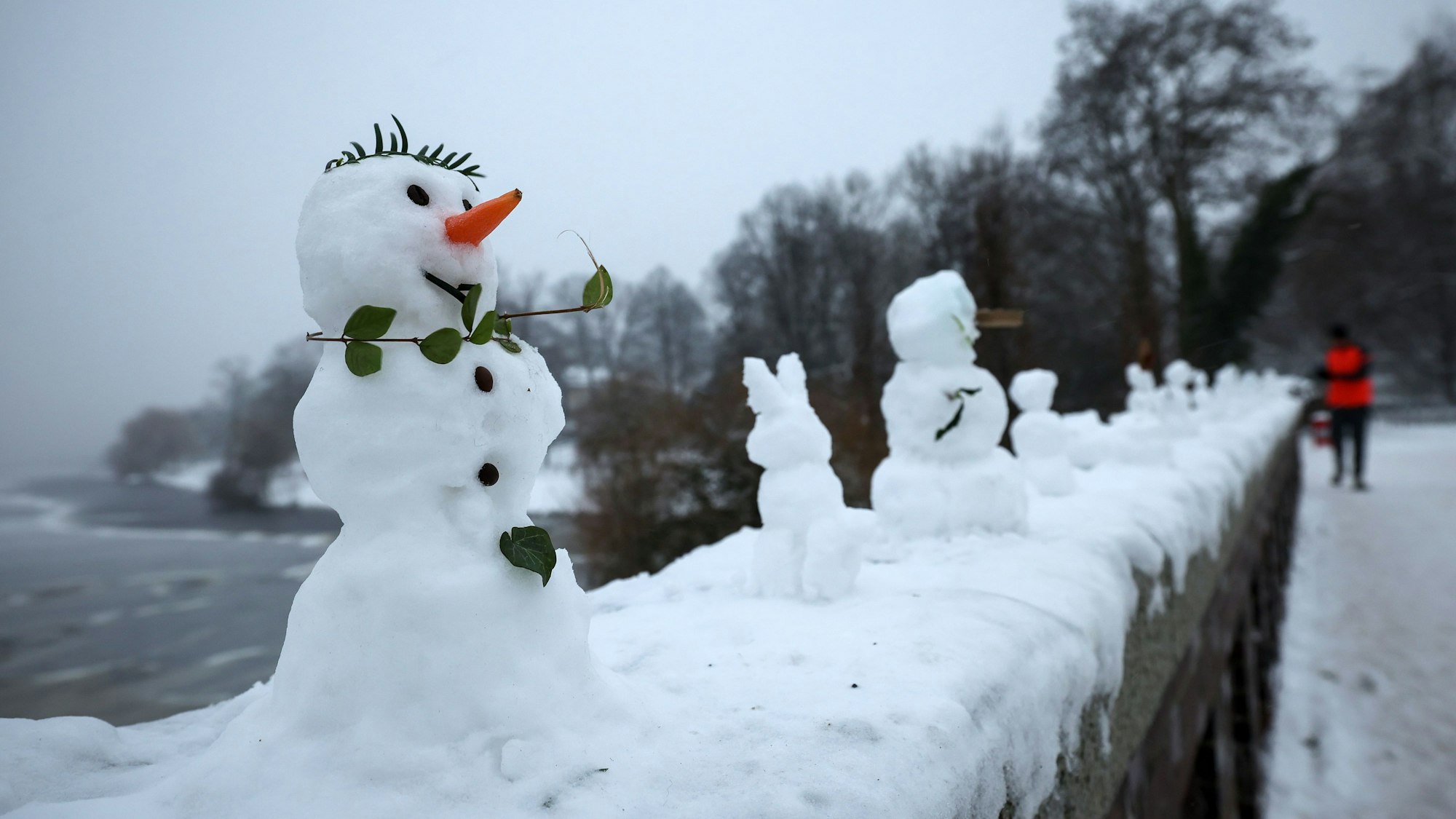 Zahlreiche kleine und winzige Schneefiguren stehen auf einer Mauer.