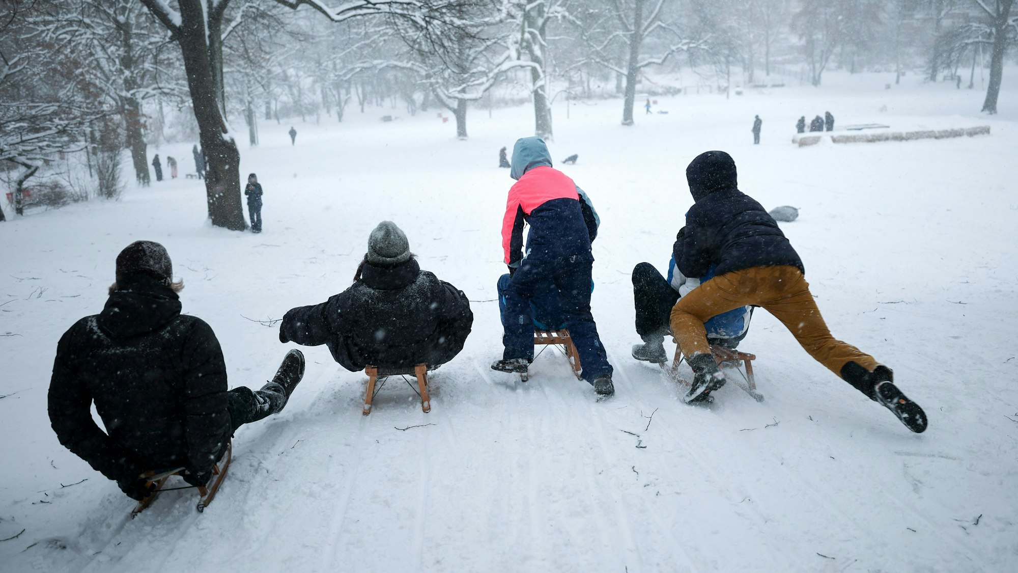 Junge Menschen rutschen mit ihren Schlitten von einem kleinen Hügel.