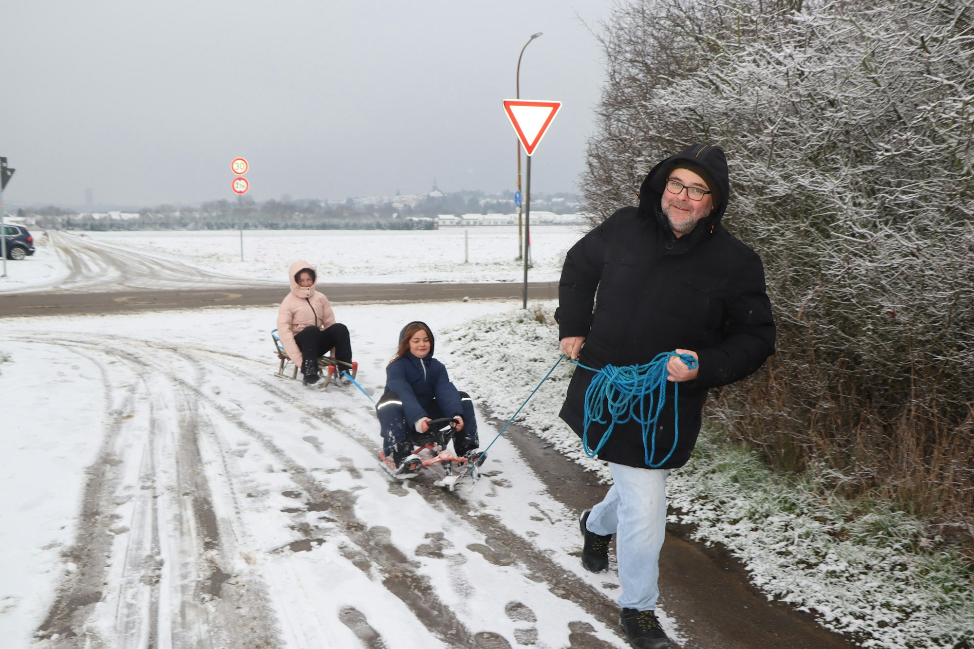 Das Bild zeigt einen Mann, der seine Töchter auf Schlitten durch den Schnee zieht.