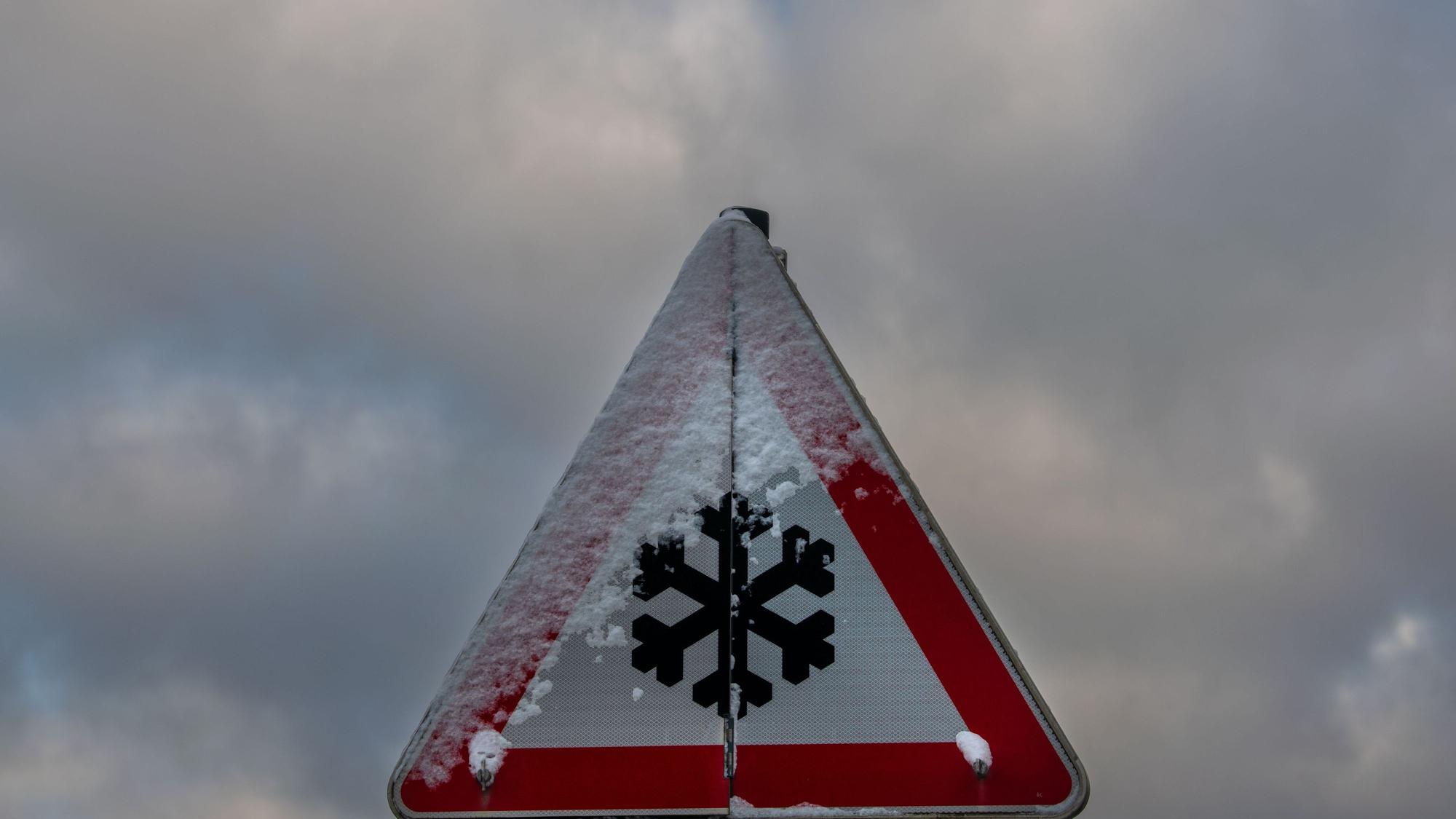 ARCHIV - 25.11.2023, Bayern, Hofolding: Ein teilweise verschneites Schild warnt vor Straßenglätte. (zu dpa: «DWD warnt vor Glatteis - Unfälle im Norden») Foto: Stefan Puchner/dpa +++ dpa-Bildfunk +++