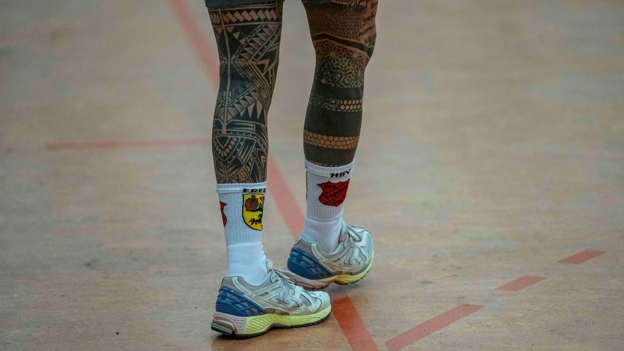 Die Beine des Frechener Trainers sind von oben bis unten tätowiert. An den Füßen hat er Socken mit Vereinslogo.
