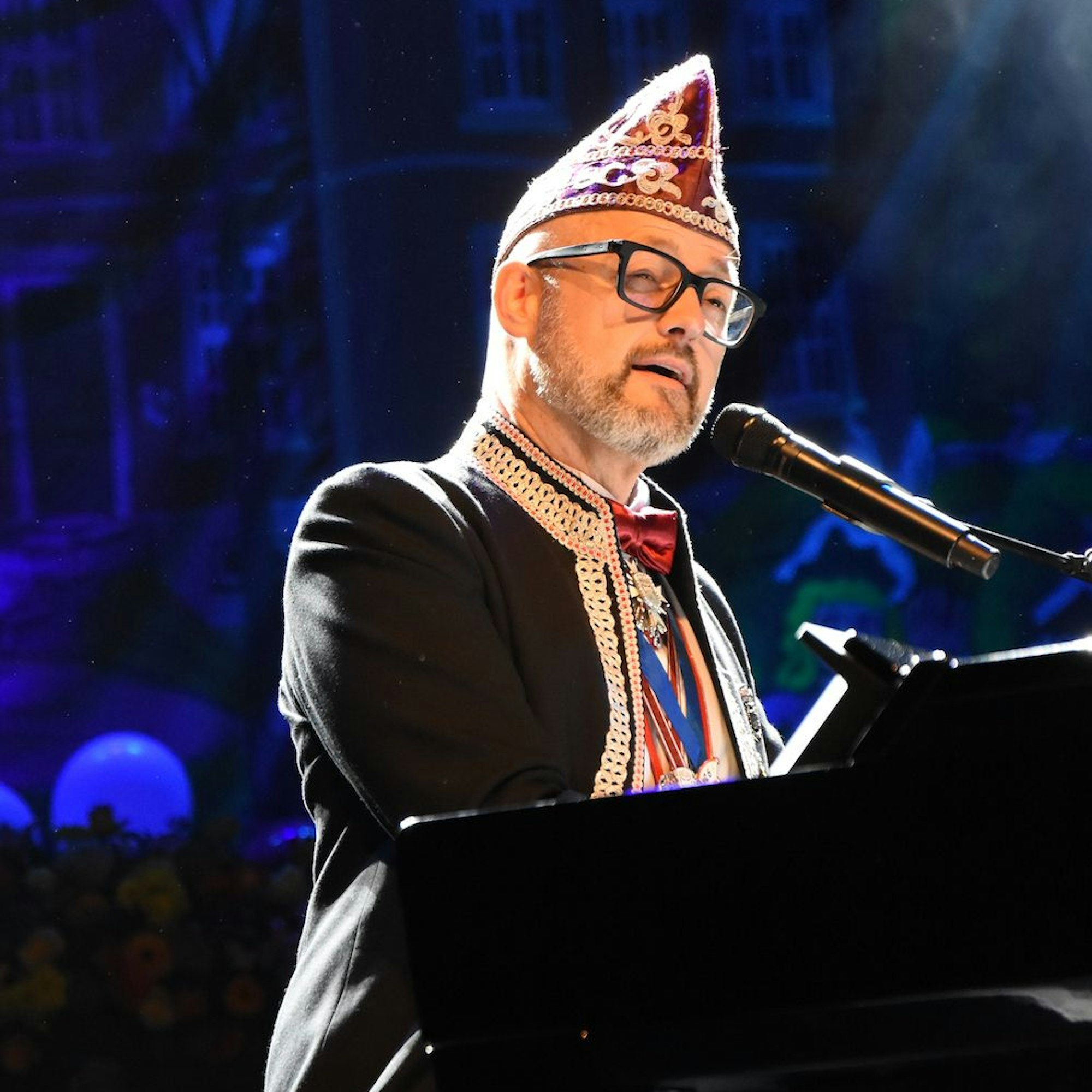 Ein Mann mit Karnevalskappe an einem Flügel.