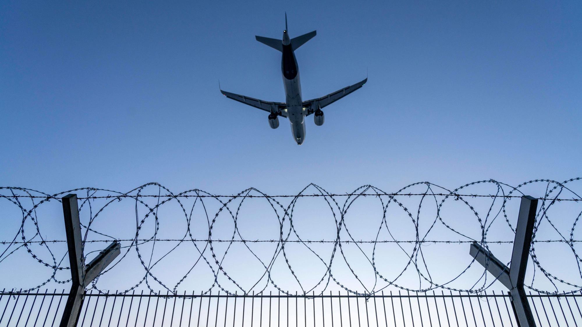 Symbolbild Sicherheit auf dem Flughafen, äußerer Zaun am Airport Düsseldorf International, Stahldrahtzaun, mit S-Draht Rollen, NATO-Draht, auf der Zaunkrone, Flugzeug im Landeanflug, Sonnenuntergang, NRW, Deutschland, Sicherheit Flughafen *** Symbolic image security at the airport, outer fence at Düsseldorf International Airport, steel wire fence, with S wire rolls, NATO wire, on the fence top, airplane approaching, sunset, NRW, Germany, airport security
