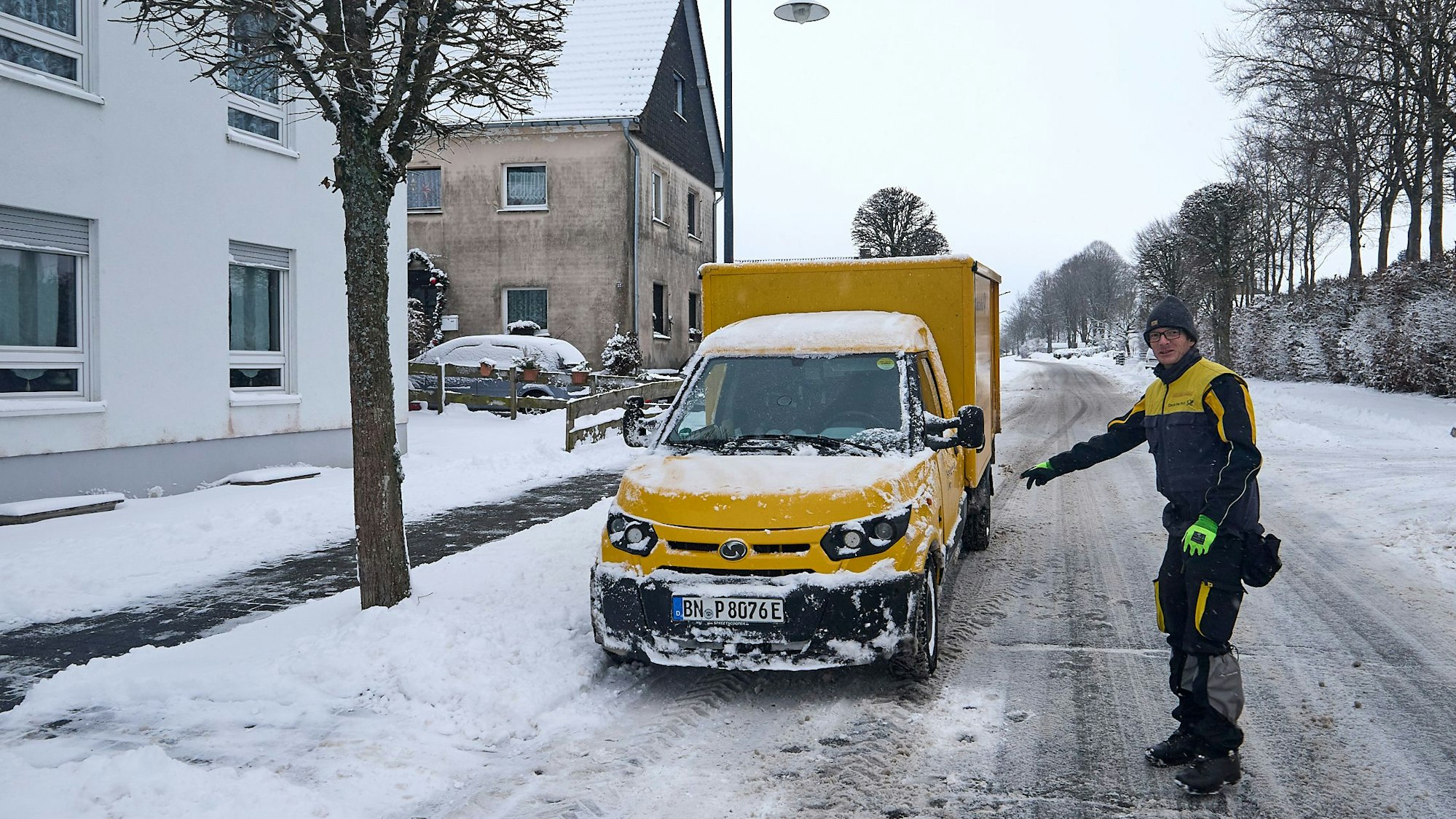 Ein Zusteller der Post geht über eine schneebedeckte Straße zu seinem elektrischen Zustellfahrzeug.
