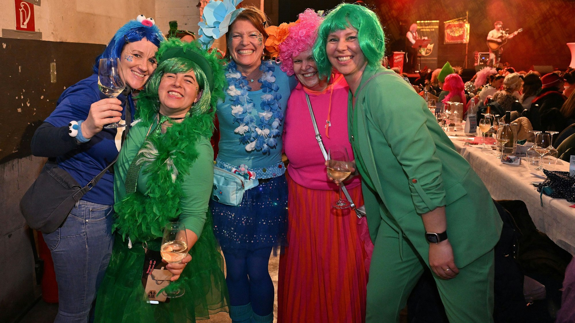 Fünf Frauen in bunten Karnevalskostümen und bunten Perücken stehen lachend zusammen