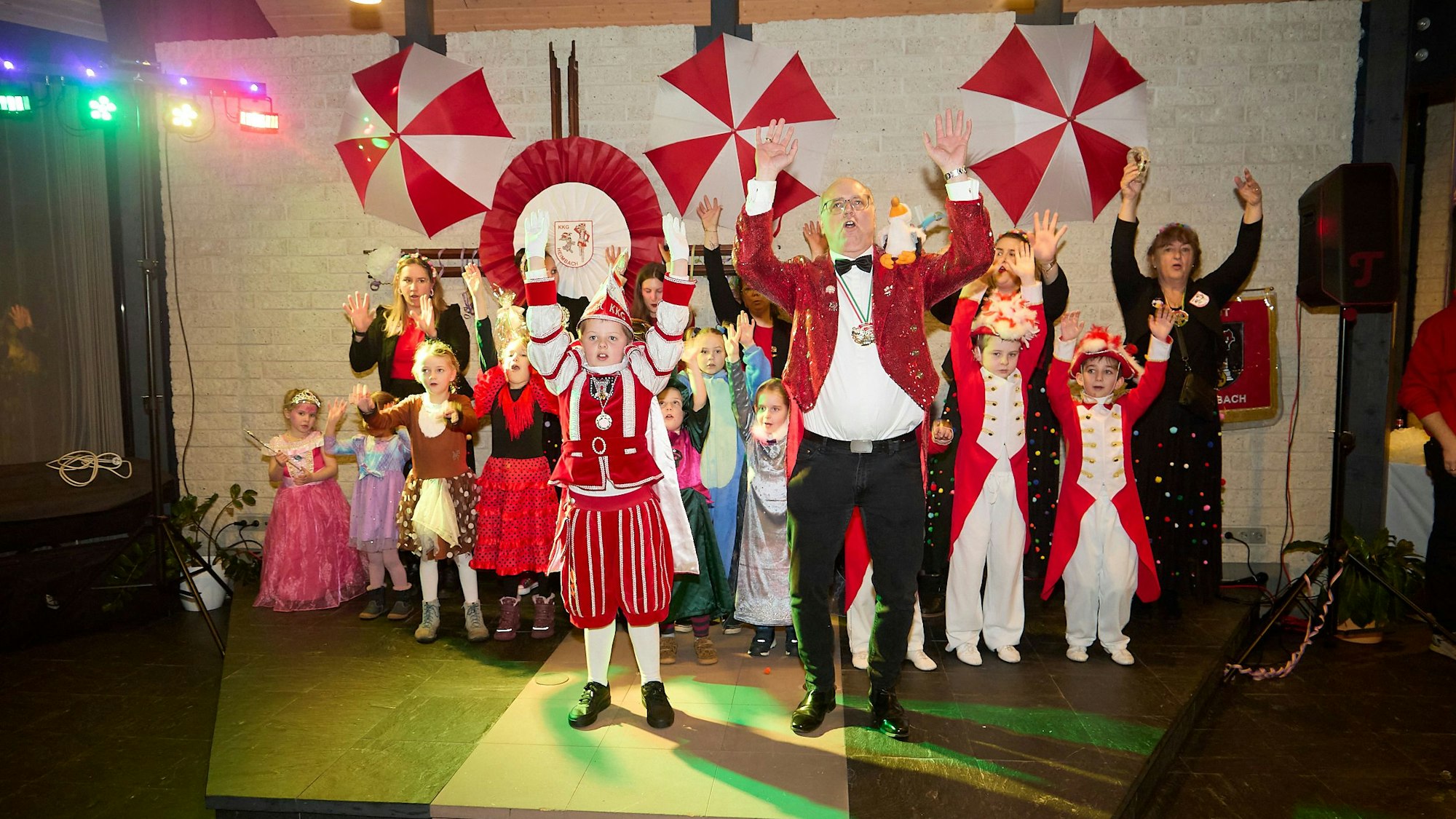 Kostümierte Kinder und Erwachsene stehen neben- und hintereinander auf der Bühne und halten die Arme nach oben.