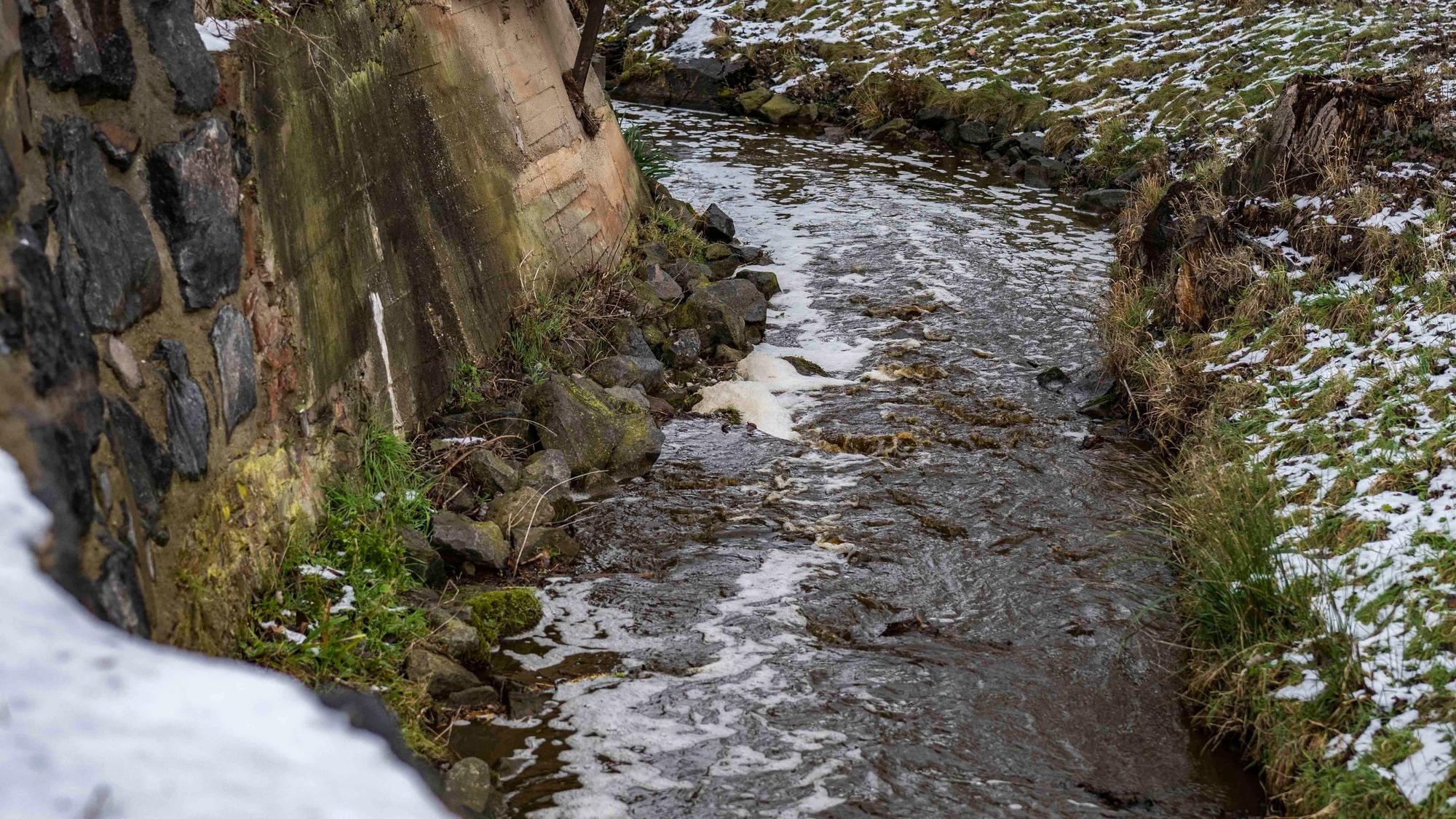 Das Bild zeigt einen Teil des Veybachs in Breitenbenden. Auf der Wasseroberfläche treibt Schaum.