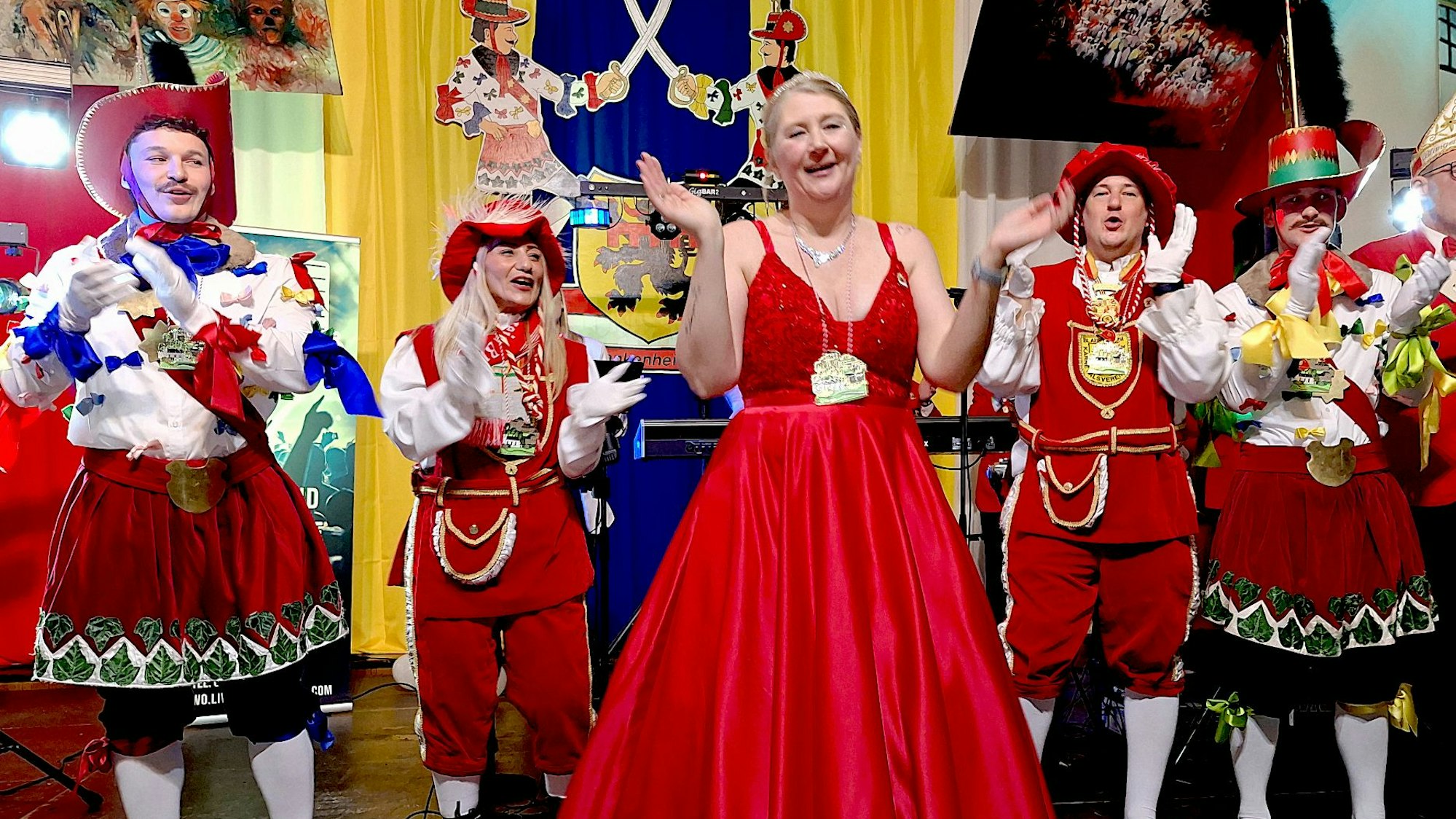 Eva Walber steht in der Mitte in einem roten Kleid, umgeben von Männern und Frauen in roten Kostümen.