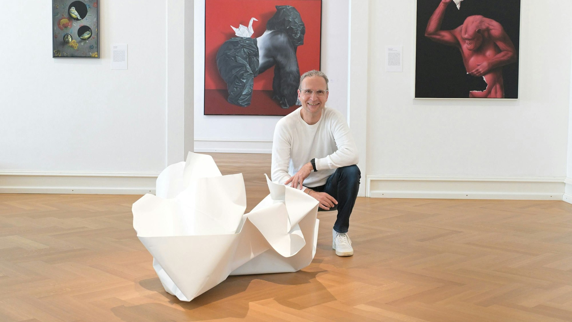Eckart Hahn kniet auf dem Boden des Museums neben einer Skulptur aus Papier.
