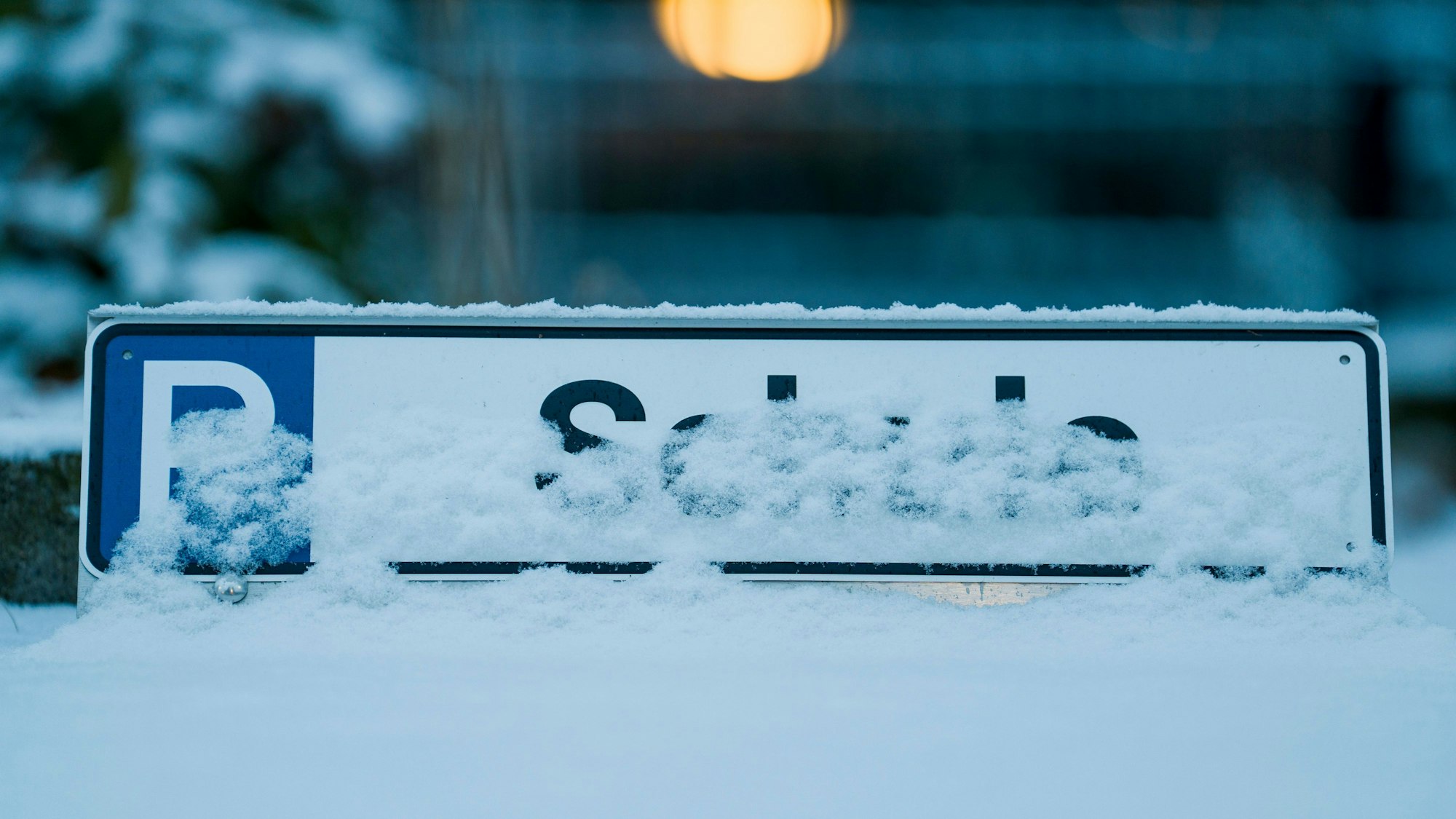 Zu sehen ist eine eingeschneite Parkplatzmarkierung mit der schlecht lesbaren Aufschrift „Schule“.