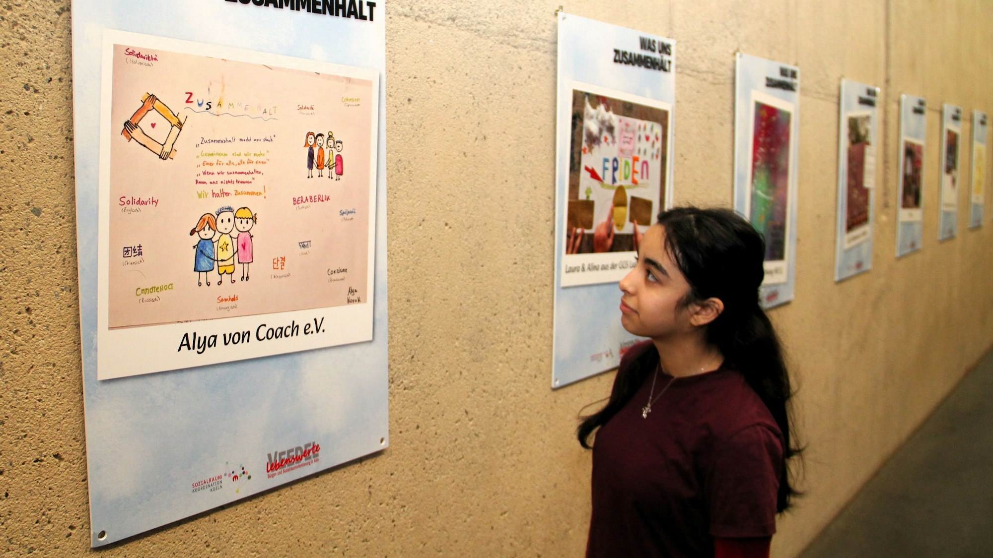 Ein Mädchen mit dunklem Haar schaut auf ein Plakat.