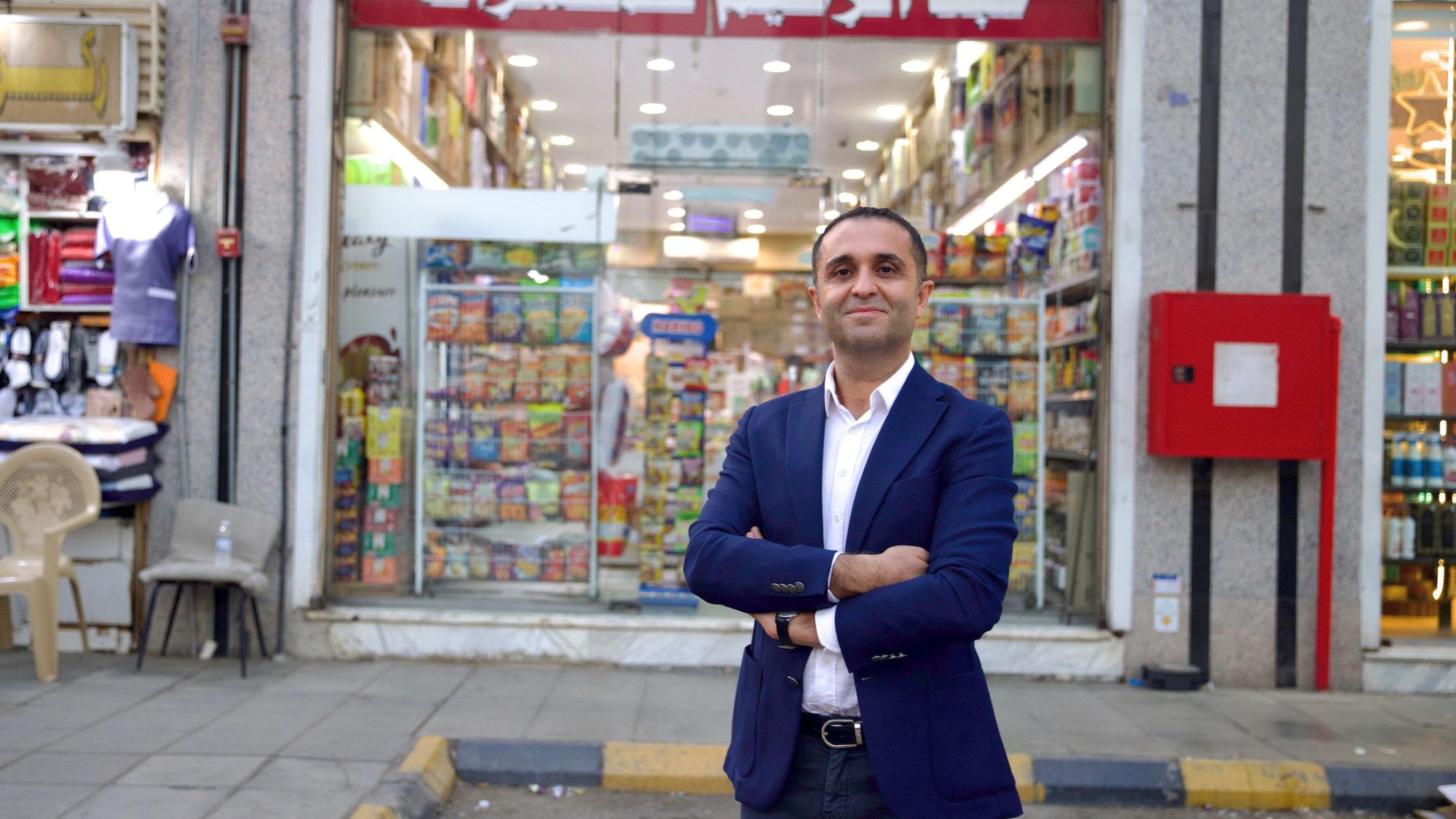 Çağdaş Kardeş steht mit verschränkten Armen vor einem Lebensmittelgeschäft und lächelt in die Kamera