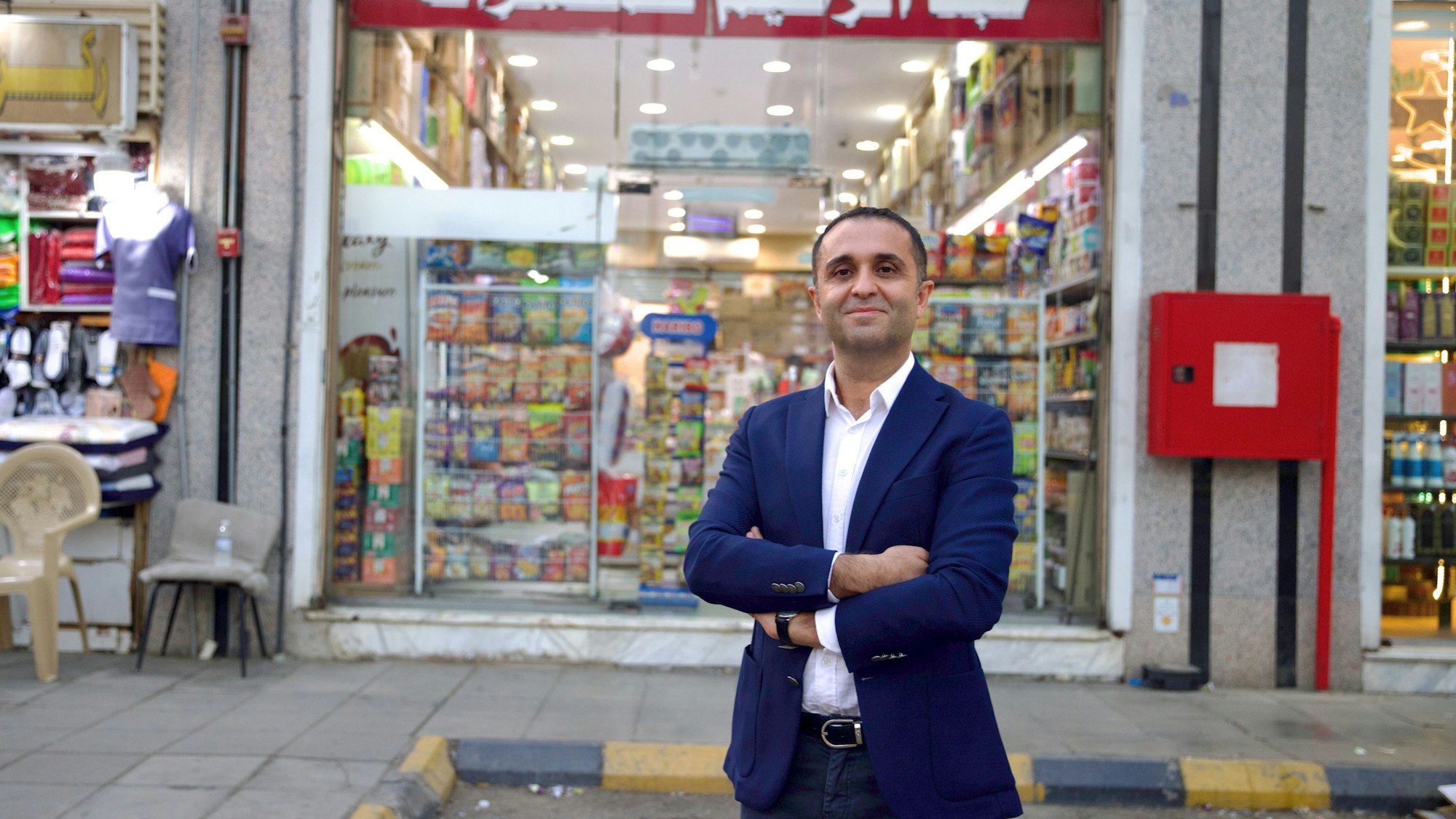 Çağdaş Kardeş steht mit verschränkten Armen vor einem Lebensmittelgeschäft und lächelt in die Kamera