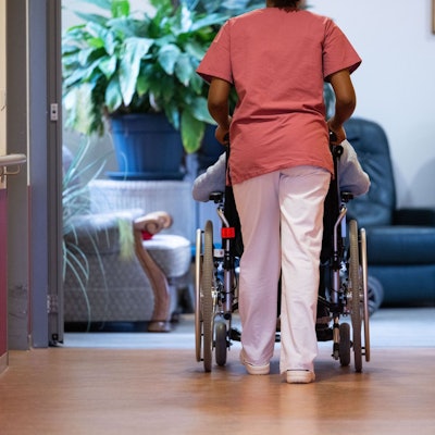 Eine Person im Rollstuhl wird von einer anderen durch einen Gang geschoben.