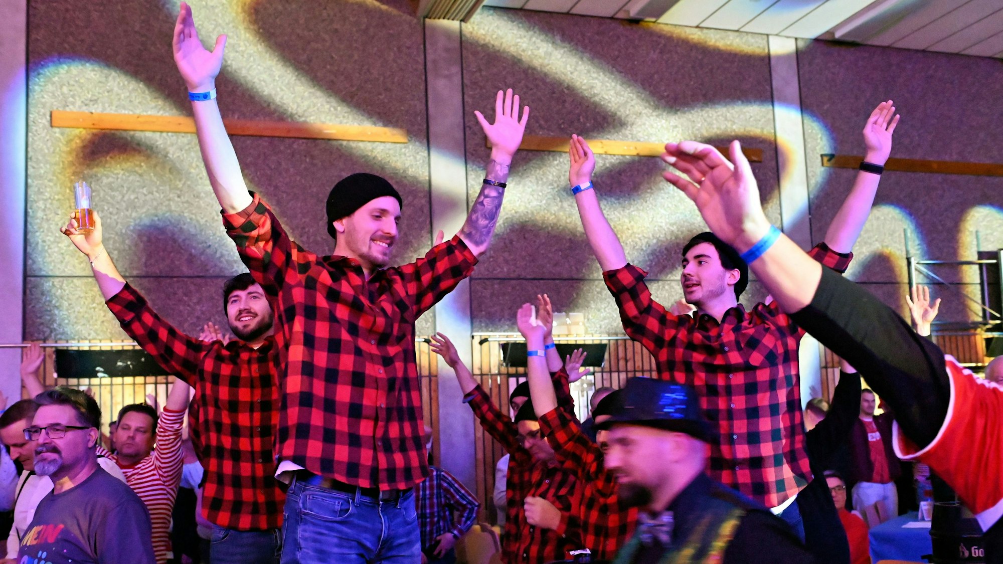 Blick ins Publikum der Weilerswister Herrensitzung: Stehende Männer in karierten Hemden heben ausgelassen die Hände in die Luft.