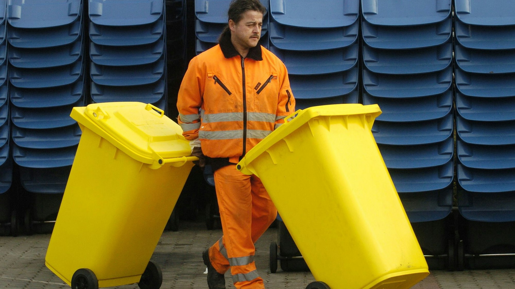 Ein Mitarbeiter eines Abfallwirtschaftsbetriebs schiebt zwei Gelbe Tonnen.