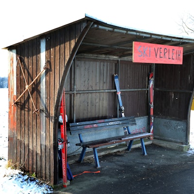 In einem Buswartehäuschen in Rösrath-Stöckchen stehen Ski und ein Rodelbob, ein Schild trägt die Aufschrift „Ski-Verleih“.