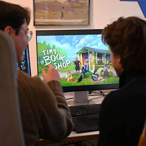 Die Computerspiele-Entwickler David Zapfe-Wildemann und Raven Rusch von dem Kölner Independent-Gamingstudio Neoludic sitzen in ihrem Büro vor einem Bildschirm, auf dem die Startseite des Spiels Tiny Bookshop zu sehen ist.