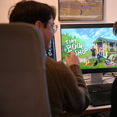 Die Computerspiele-Entwickler David Zapfe-Wildemann und Raven Rusch von dem Kölner Independent-Gamingstudio Neoludic sitzen in ihrem Büro vor einem Bildschirm, auf dem die Startseite des Spiels Tiny Bookshop zu sehen ist.