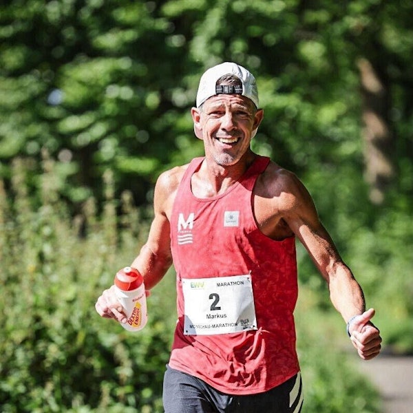 Markus Mey trägt beim Laufen eine Kappe mit dem Schirm nach hinten und hält in einer Hand eine Trinkflasche.