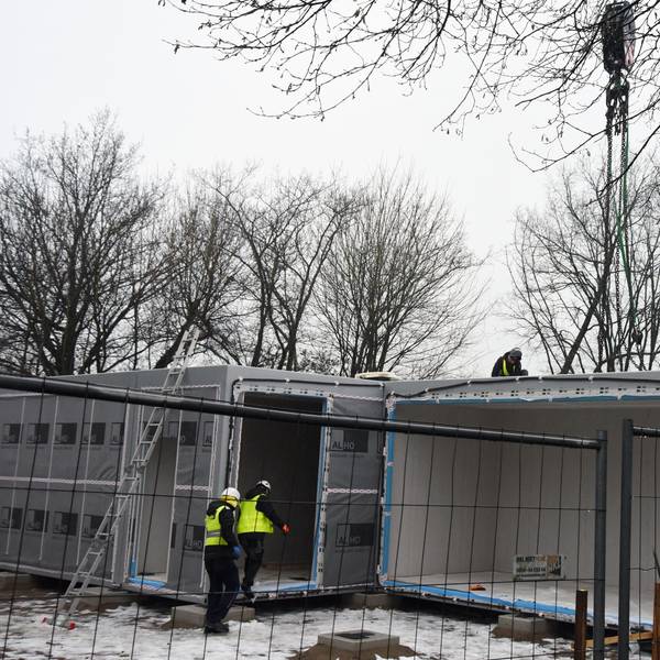 Mehrere Arbeiter stellen Container auf einem Schulhof auf.