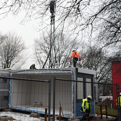 Mehrere Arbeiter stellen Container auf einem Schulhof auf.