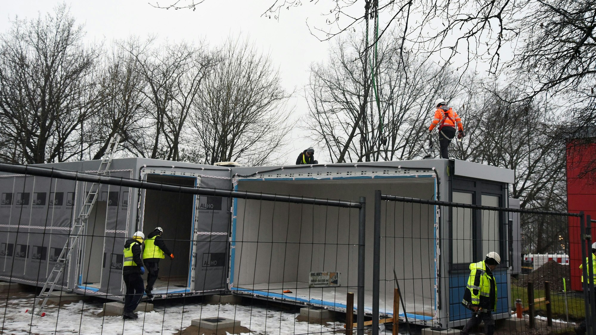 Mehrere Arbeiter stellen Container auf einem Schulhof auf.