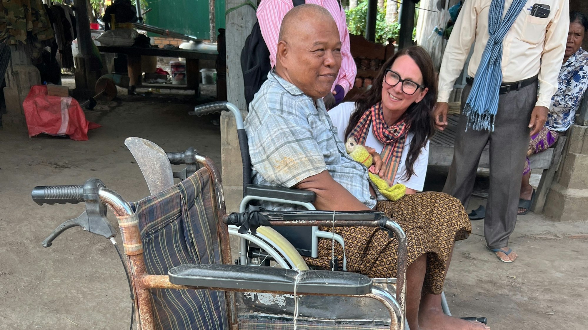 Ein älterer Herr aus Kambodscha sitzt in einem neuen Rollstuhl, daneben steht sein alter, verrosteter Rollstuhl.