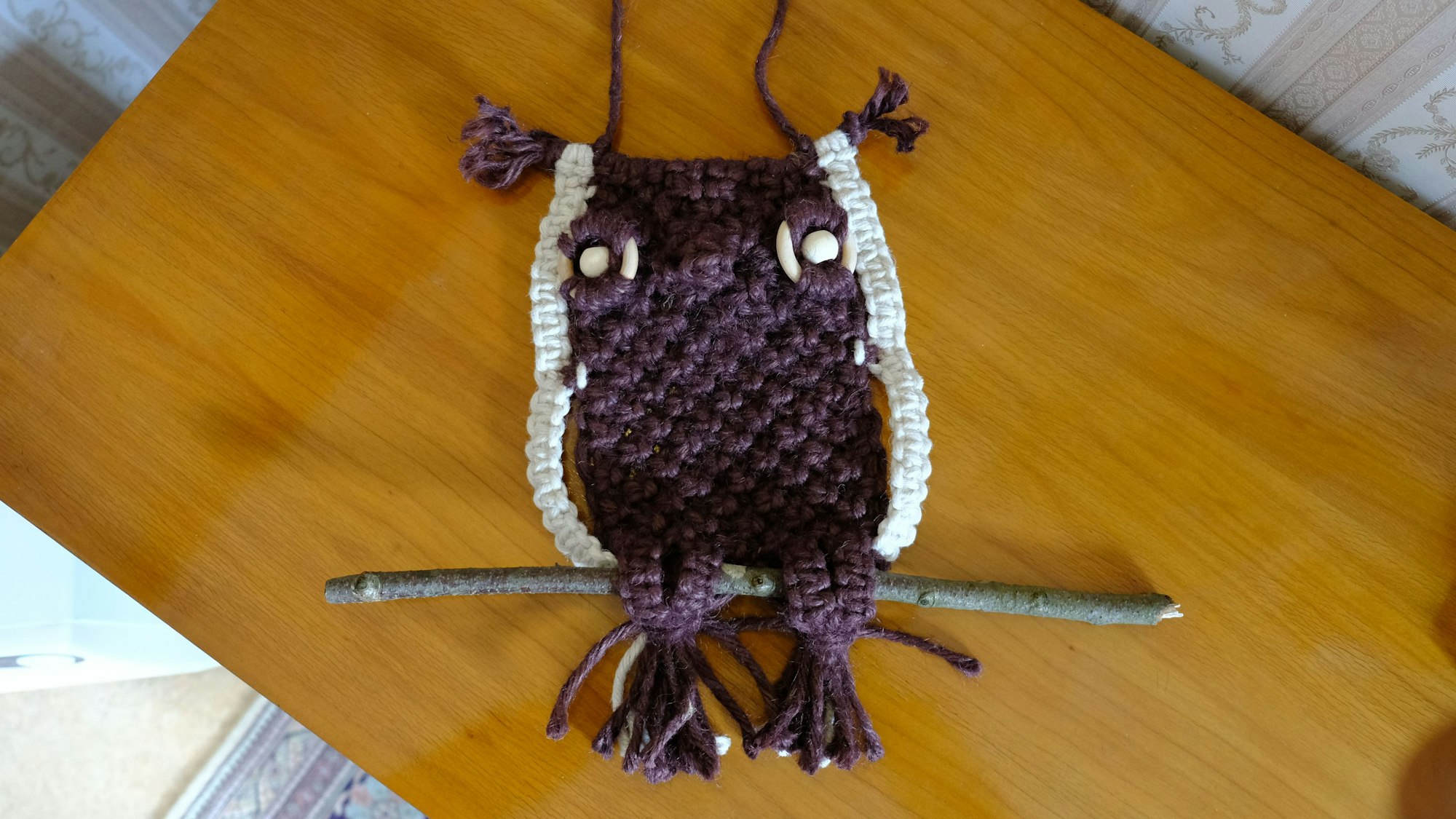 Eine aus braunem Garn in Makramee-Technik gefertigte Eule sitzt auf einem Ast.