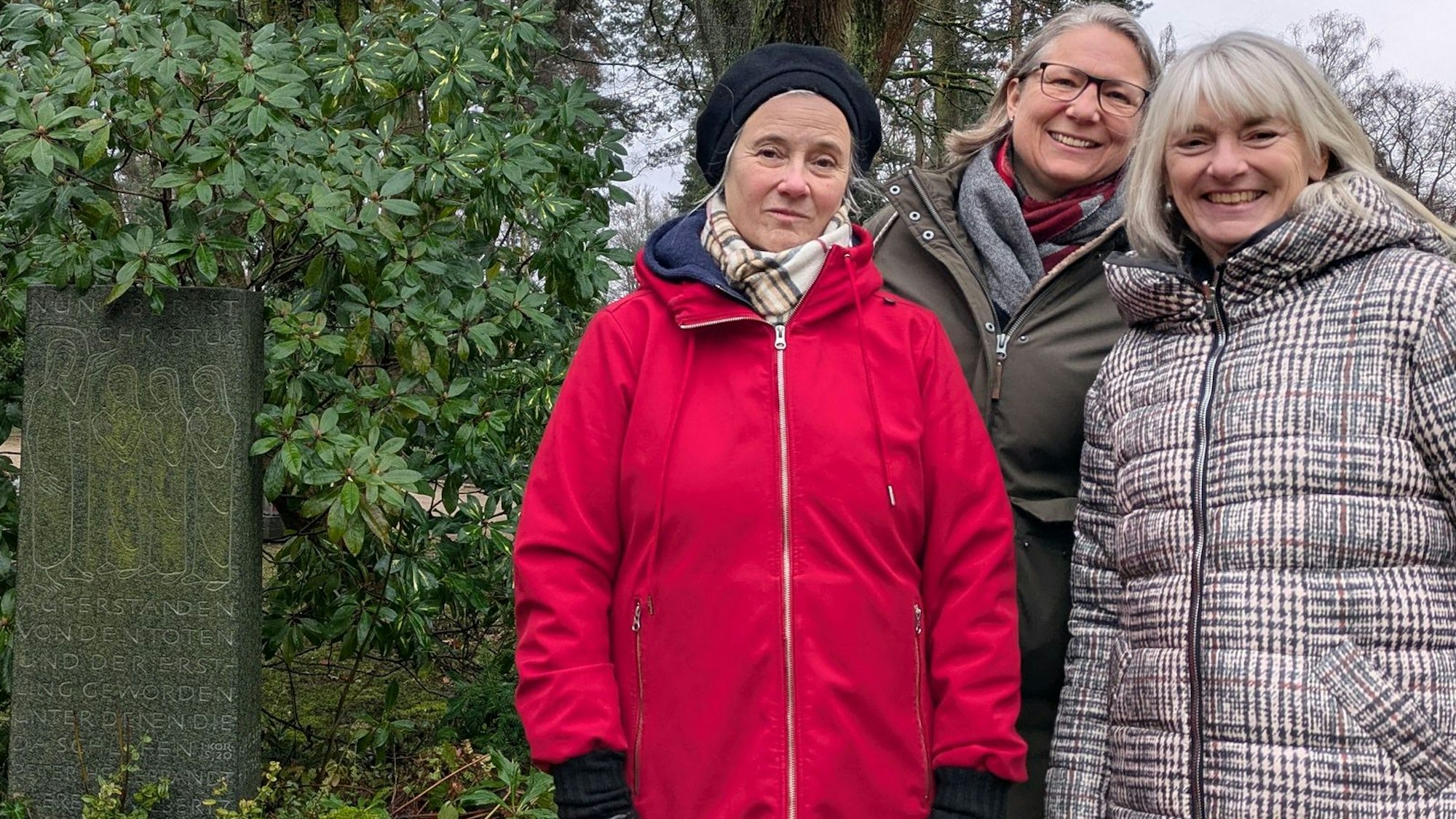 Drei Frauen stehen an einem Grabstein.