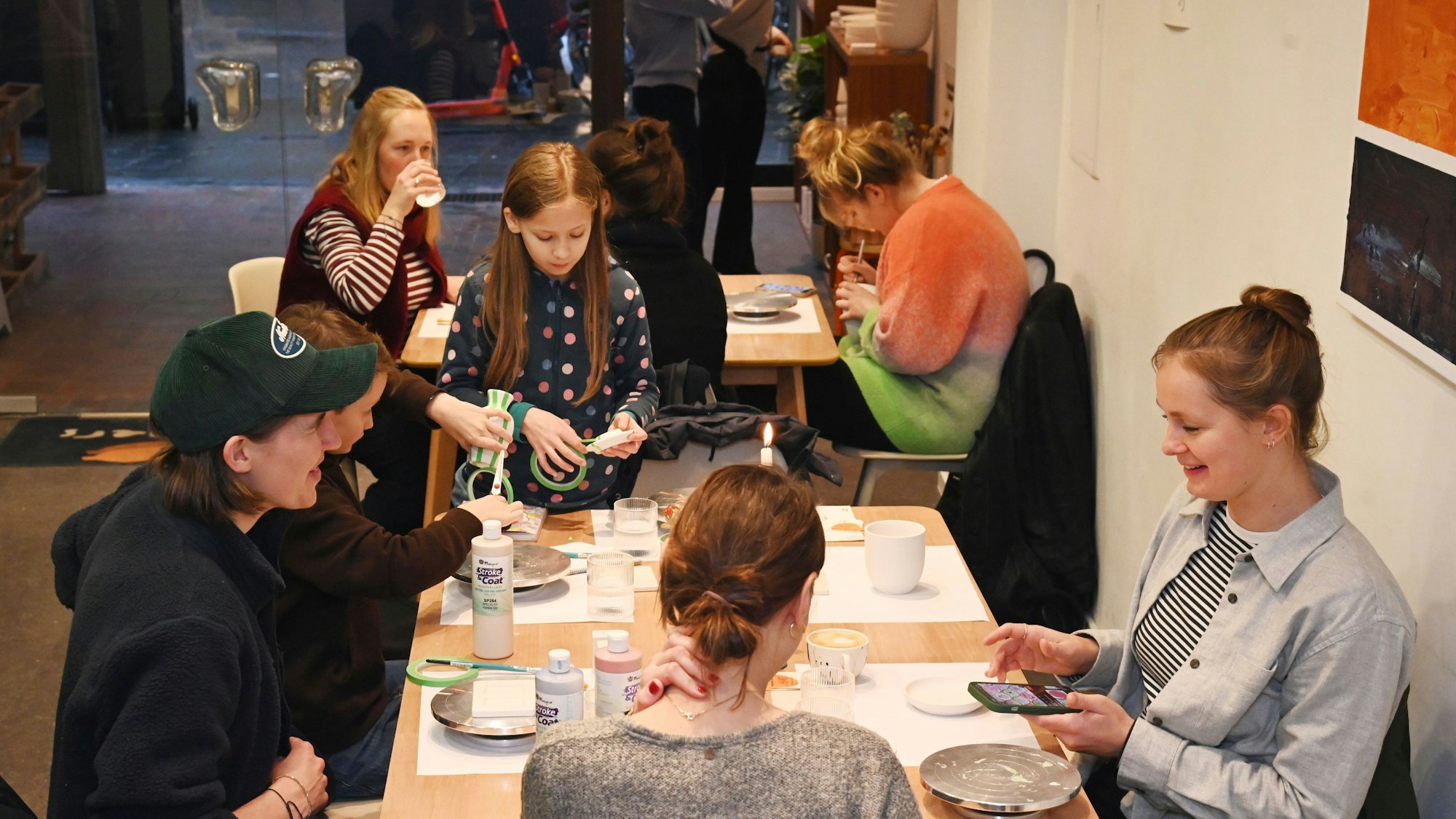 Acht Menschen sitzen an Tischen und bemalen ihre Keramik.